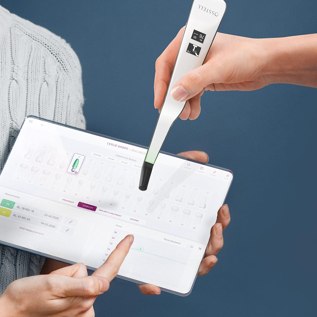 Person holding an iPad-like prototype showing Osstell Connect. Hand holding Ostell's instrument that measures stability in implants.